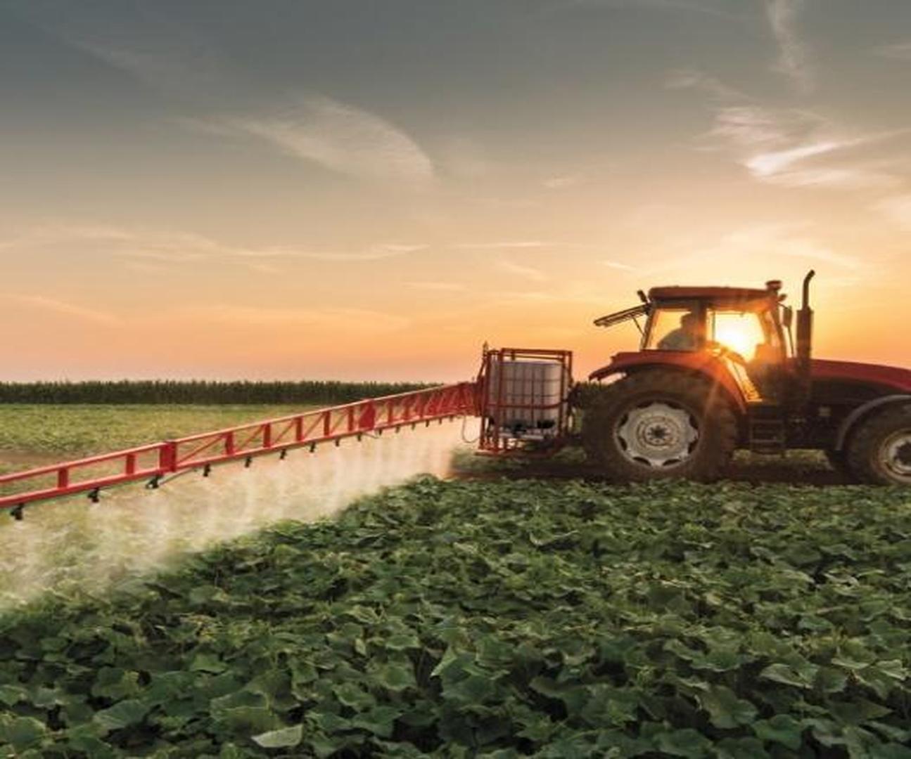 Tractor spraying crops in a field during sunset.