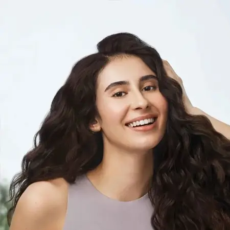 A smiling woman with long curly hair and a light purple top.